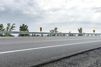 a paved road with yellow traffic signs on the side and trees in the background on a cloudy day