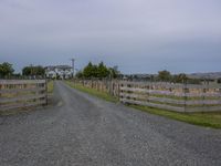 a small gravel road with a barn in the middle of it and an attached gate