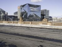 the modern looking building has many windows on both sides of it and a small sidewalk is surrounded by snow on the pavement