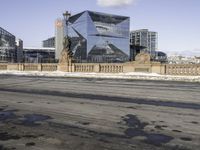 the modern looking building has many windows on both sides of it and a small sidewalk is surrounded by snow on the pavement