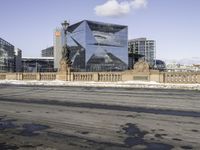 the modern looking building has many windows on both sides of it and a small sidewalk is surrounded by snow on the pavement