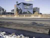 the modern looking building has many windows on both sides of it and a small sidewalk is surrounded by snow on the pavement