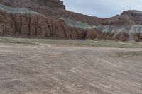 an empty field next to a big mountain with rocks in the background of the picture