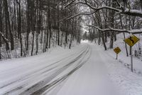 a snowy and icy road in a wood area with a sign saying caution is ahead