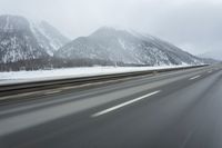 a freeway near some mountains and trees during the snow in wintertime in a blurry effect
