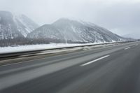 a freeway near some mountains and trees during the snow in wintertime in a blurry effect