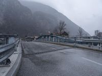 the bridge is empty during the rainy day on the mountainside road below, and houses in the background