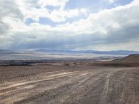 a view of the barren mountains and a dirt road in front of a cloudy sky