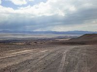 a view of the barren mountains and a dirt road in front of a cloudy sky