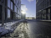 the sun is shining on the road in the city in winter time by a glass building