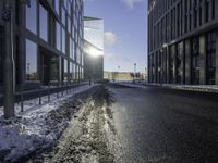 the sun is shining on the road in the city in winter time by a glass building