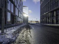 the sun is shining on the road in the city in winter time by a glass building