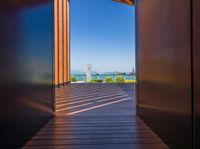 open doors on a walkway overlooking an ocean with buildings in the distance and blue skies