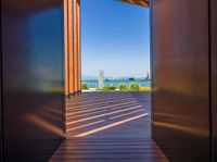 open doors on a walkway overlooking an ocean with buildings in the distance and blue skies