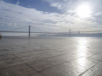 the sun shines brightly across a bridge and body of water at the top of it