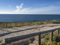 a long wooden railing near a beach with blue water and clouds in the background at dawn