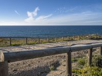 a long wooden railing near a beach with blue water and clouds in the background at dawn