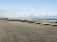 an empty street near the beach with a fence and sand in the background and fog