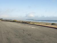 an empty street near the beach with a fence and sand in the background and fog