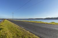 a empty road beside the water and on the other side of a small lake with power lines overhead