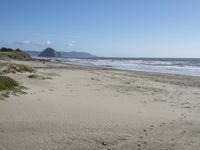 an empty, sandy beach with sea and mountains in the background and sky with only one cloud