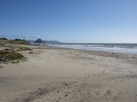 an empty, sandy beach with sea and mountains in the background and sky with only one cloud