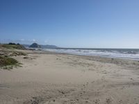 an empty, sandy beach with sea and mountains in the background and sky with only one cloud