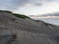 a person walking up a beach carrying a surfboard over sand dunes next to the ocean