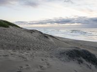 a person walking up a beach carrying a surfboard over sand dunes next to the ocean