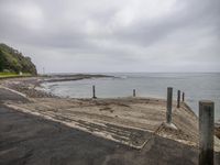 a beach side with gravel pathway next to ocean with rocks and fence posts in the foreground