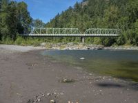 two people are standing near the water and a bridge with green bridges over it,