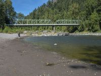 two people are standing near the water and a bridge with green bridges over it,