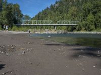 two people are standing near the water and a bridge with green bridges over it,