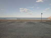 a empty parking lot in front of the ocean and beach with a blue sky above