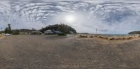 an empty sandy lot near a beach and ocean, and a sky full of clouds