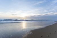 a picture of a beach in the morning, with footprints in the sand on the shore