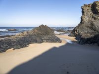 a man walking down the sand toward rocks by the ocean at low tide with an umbrella on top