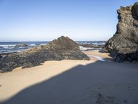 a man walking down the sand toward rocks by the ocean at low tide with an umbrella on top