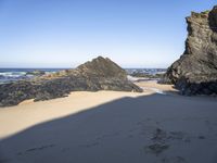 a man walking down the sand toward rocks by the ocean at low tide with an umbrella on top