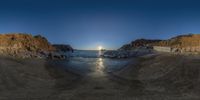 a fish eye image of a beach during sunset with two boats in the ocean and the cliffs in the background