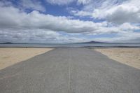 a paved beach lined with a line of water and hills in the distance, in the foreground is the sky