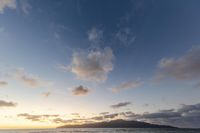 people are standing on the beach in front of water and mountains, looking at a sunset