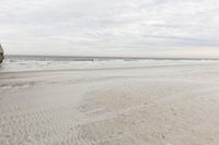 an ocean beach with water and rocks on it, and two people walking on the beach