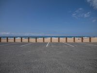 a person walking along the beach next to a fence, with ocean in background and people on the beach