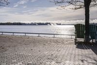 a bench and chair sitting on the curb by the water with benches to sit and watch