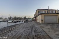 the boardwalk leading to a building has boats and people standing on it near by buildings