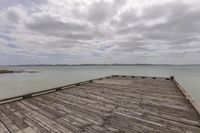 a boardwalk extends to an ocean, with a dock and a cloudy sky in the distance