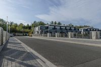 an empty road with a fenced in building behind it and a white van parked at the side