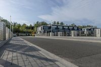 an empty road with a fenced in building behind it and a white van parked at the side