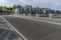 an empty road with a fenced in building behind it and a white van parked at the side